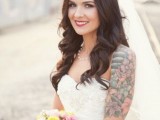 a strapless lace applique wedding dress with no sleeves shows off the bride’s tattoo on the shoulder and arm