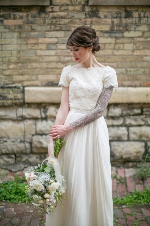 a beautiful wedding dress with a lace bodice and sleeves that show off the bride's tattoo sleeve, a pleated skirt