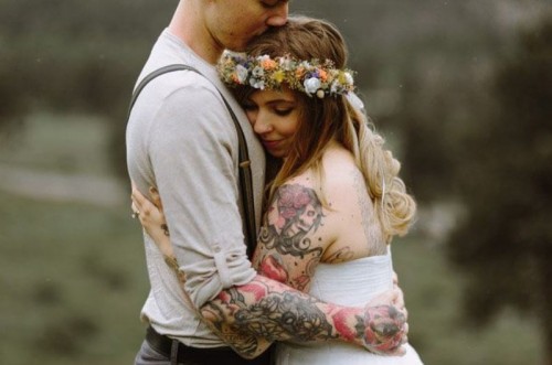 a strapless wedding dress lets us see a large colorful tattoo on the shoulder and arm and show it off at its best