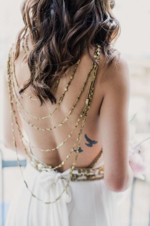 a white embellished A-line wedding dress with a cutout back and a layered gold necklace on the back that accents a small back tattoo of the bride