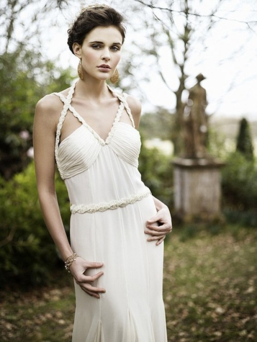 a neutral pleated and draped sheath wedding dress with am embellished sash and straps on the bodice