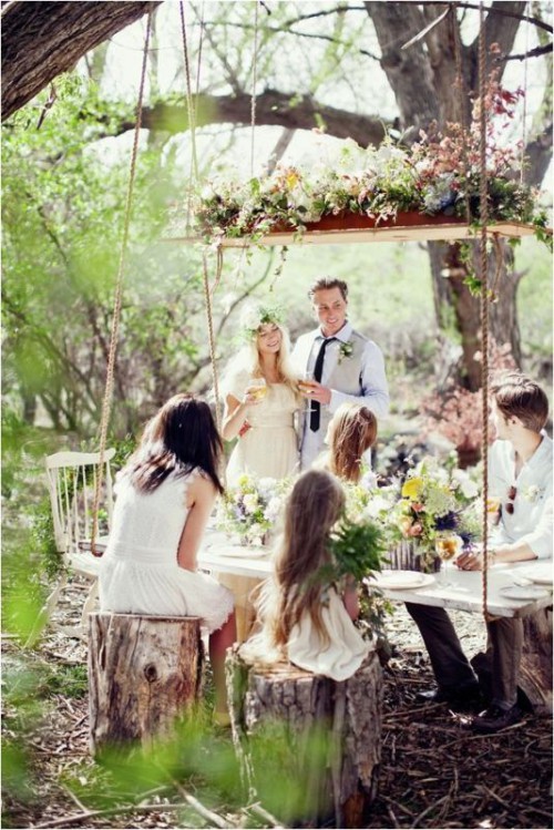 a rustic overhead floral decoration of a wooden board and greenery and some dark blooms for a relaxed reception