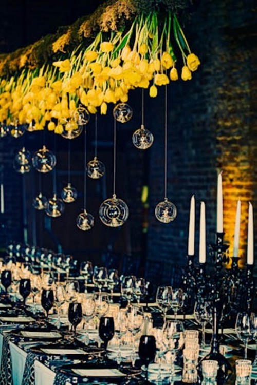 a bold overhead wedding decoration of bright yellow tulips hanging down and clear candleholders with candles
