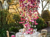 a bright and lush floral chandelier of bold red, pink, purple and blush blooms that touches the table and acts as a centerpiece, too