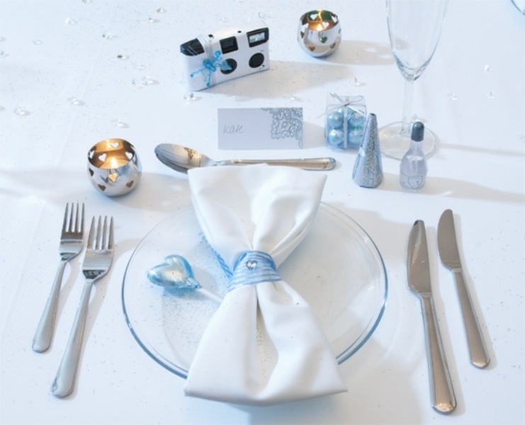 A beautiful silver and ice blue winter wedding place setting with a ice blue ornaments, an ice blue glass plate, ribbons and salt and pepper