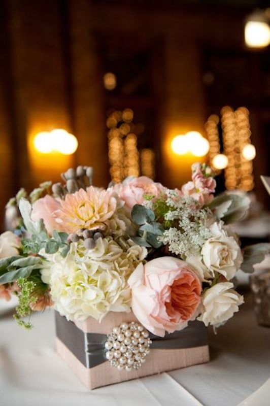a refined wedding centerpiece of a pink box and a vintage brooch, pink and neutral blooms and greenery is chic