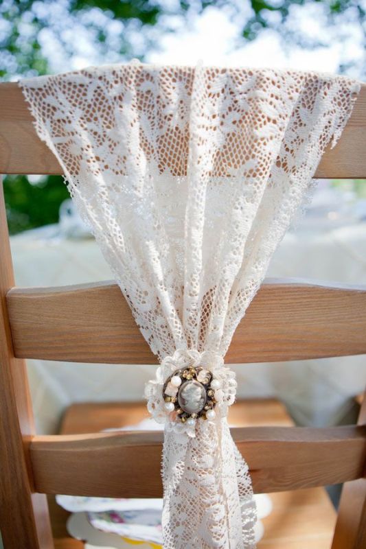 a lace wedding chair cover with a vintage brooch is a stylish decoration for a wedding chair, a chic idea for a vintage wedding