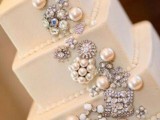 a white square wedding cake decorated with vintage brooches and pearls is a chic and bold idea for a glam or vintage wedding