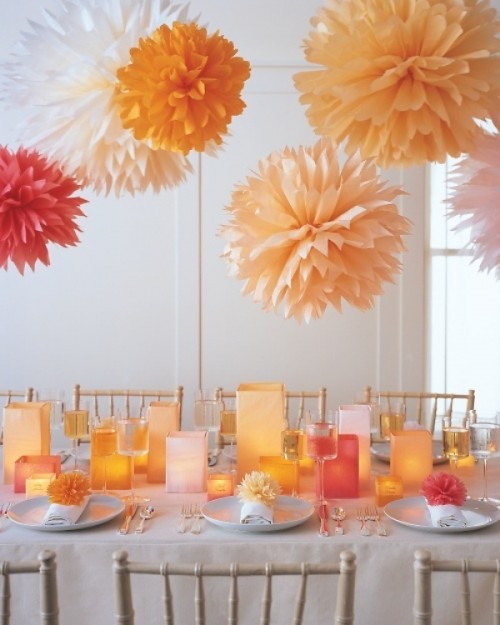 bright yellow, orange, red and white paper pompoms over the table match the square candle lanterns on the table and create a cohesive space