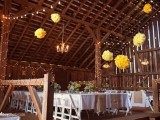 yellow paper pompoms and lights on the pillars add a sunshine feel to the barn reception space