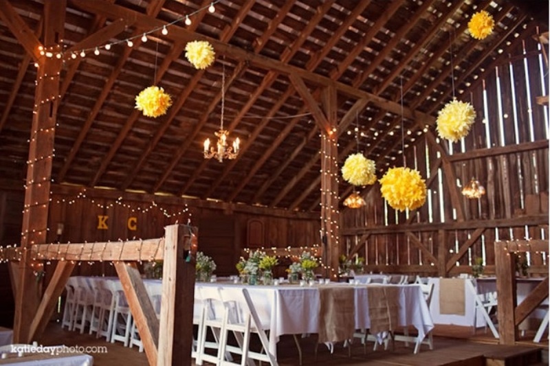 Yellow paper pompoms and lights on the pillars add a sunshine feel to the barn reception space