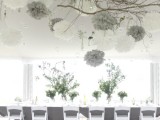 a creative overhead installation of branches, white and grey paper pompoms, crystals, candleholders and white blooms for a winter wedding
