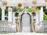 colorful paper pompoms hanging over the ceremony space make it look fun and festive, ideal for a festival-themed wedding
