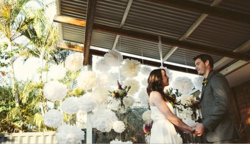 a wedding backdrop of white paper pompoms is a cool decor idea for a modern wedding with a touch of fun