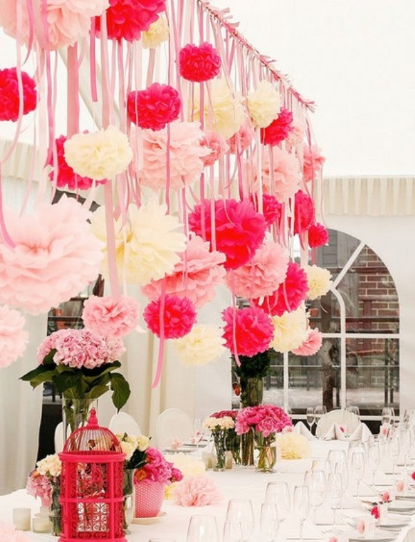 An overhead installation with pink, fuchsia and white paper pompoms and matching pink blooms on the table for a romantic feel