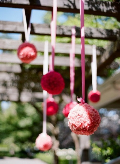 red and pink paper pompoms hanging over the reception look festive, bright and fun and add color to the space