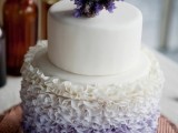 a beautiful white and lilac wedding cake with a ruffle ombre tier and some purple blooms on top
