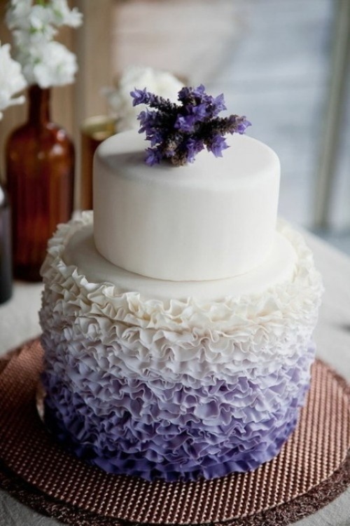a beautiful white and lilac wedding cake with a ruffle ombre tier and some purple blooms on top