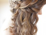 long wavy hair with a braided halo and neutral and bright blooms as a crown on top is a lovely idea for a beach or some other wedding, a rustic or a boho one