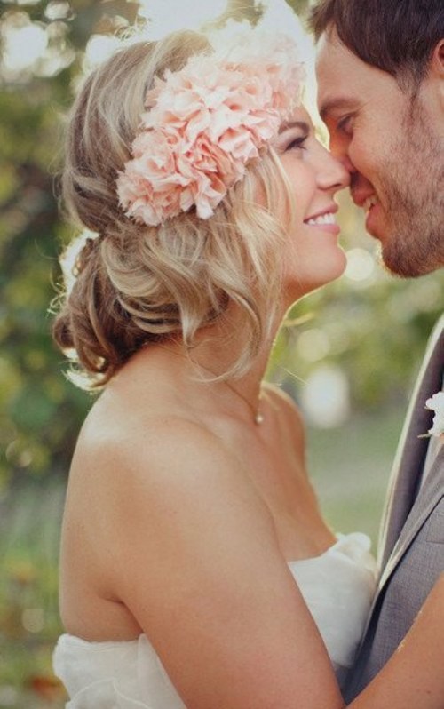 a messy and wavy low updo with some locks down and a pink floral crown is a dreamy and romantic idea for a beach bride and not only