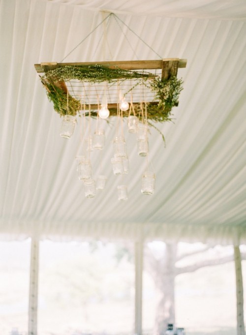 a unique woodland wedding chandelier of a wooden frame, greenery and hanging bulbs and jars
