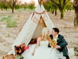 a romantic wedding picnic with a boho teepee, bright pillows, blooms, layered blankets for a boho-loving couple
