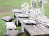 a neutral wedding picnic with a low reclaimed wood table, grey pillows, chargers, white feathers and crystal arrangements