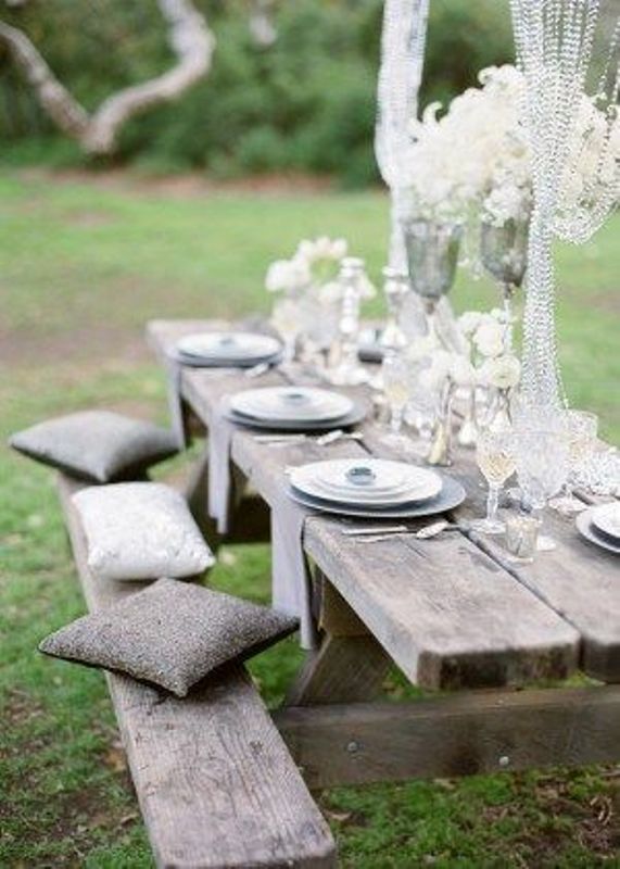A neutral wedding picnic with a low reclaimed wood table, grey pillows, chargers, white feathers and crystal arrangements