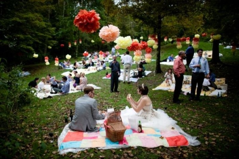 A bright wedding picnic with colorful layered blankets, bright paper pompoms and balloons and picnic baskets with food