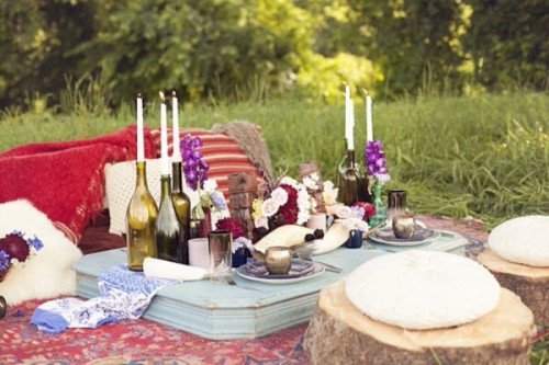 a jewel tone wedding picnic with bright blankets, colorful blooms, pillows on stumps, candles and a low table of wood
