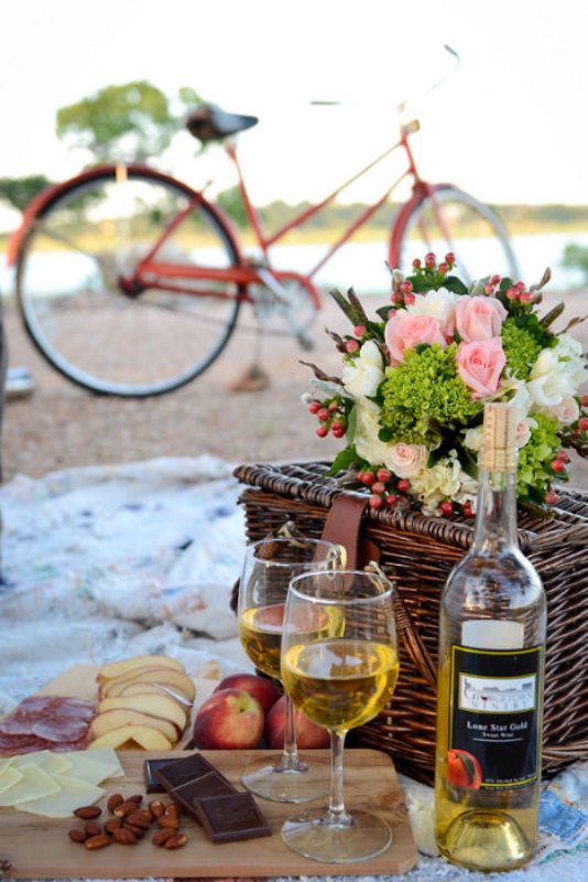 A wedding picnic with a basket, pastel blooms and greenery, apples, cheese, nuts and wine is perfect