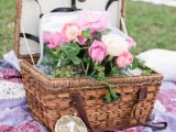 a bright picnic setting with a colorful blanket, pink blooms in a basket and a wood slice table number