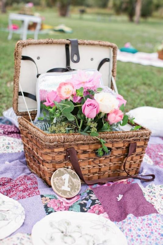 A bright picnic setting with a colorful blanket, pink blooms in a basket and a wood slice table number