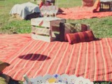 a summer picnic setting with a colorful striped blanket, pillows, a crate as a stand and a bathtub with ice for wine cooling