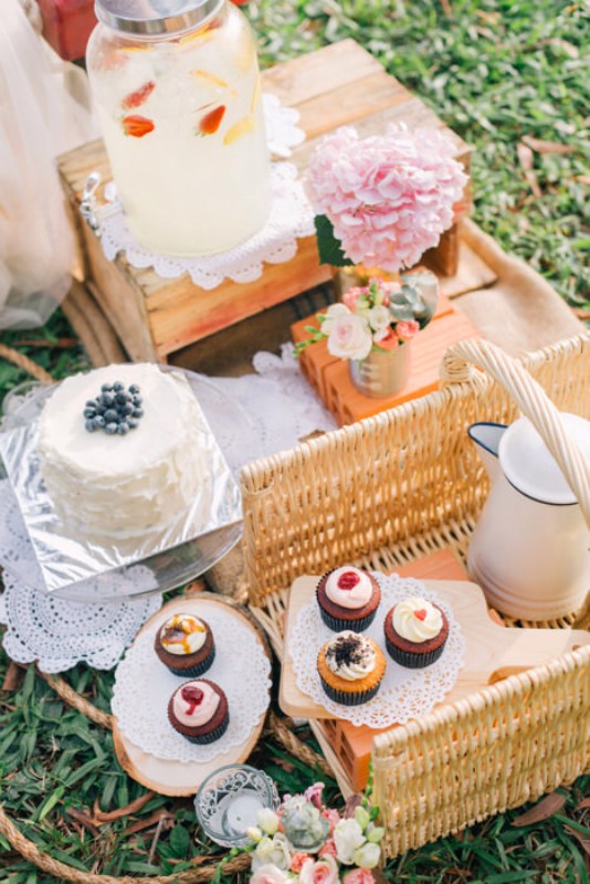 A rustic summer wedding picnic setting with crates, baskets, bright blooms, delicious sweets, lemonade and tea and coffee