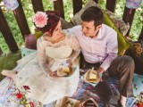 a wedding picnic on a terrace with a bright blanket and pillows, delicious food, bright blooms and lots of sweets