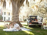a vintage rustic wedding picnic with a paper bunting, some photos on the tree, a blanket and a vintage car as a sweets table