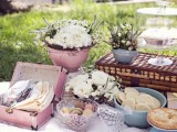 a pastel pink wedding picnic with a blanket, white blooms in pots, sweets in bowls and glass plates