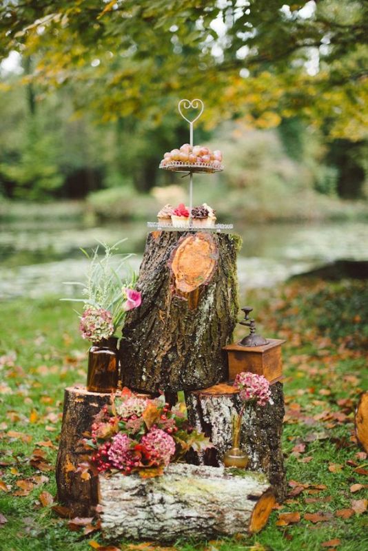 A rustic or woodland dessert display of tree stumps, bright blooms and greenery and desserts on a stand on top