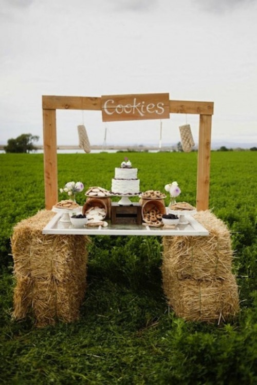 a rustic dessert table placed on hay, with a wooden frame, pink blooms and wooden baskets to hold desserts