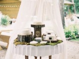 a rustic dessert display with moss on it and tree stumps and stands with a curtain over it is a cool idea