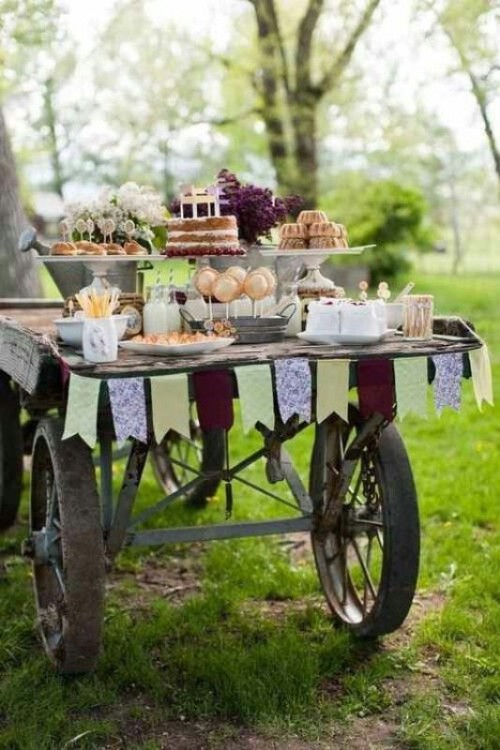 a vintage rustic dessert display - a cart with a fabric bunting, some bright blooms and a tin watering can is a very refined idea
