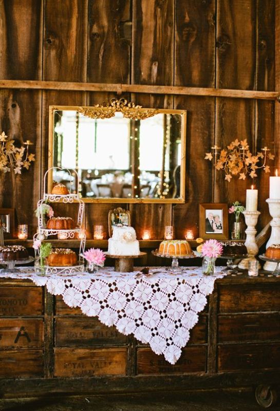 A vintage rustic dessert table made of rough wooden crates, with a doily tablecloth, candles and a vintage mirror in front of it