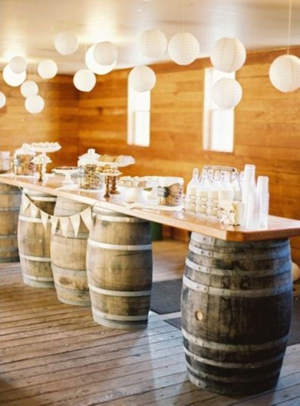 A rustic dessert and drink display of wine barrels and a tabletop on them, various sweets and milk bottles