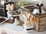 a rustic vintage dessert display of a table with crates and vintage white stands for food plus a bunting with fabric flowers