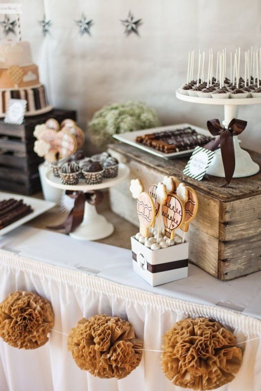 A rustic vintage dessert display of a table with crates and vintage white stands for food plus a bunting with fabric flowers