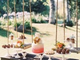 a rustic dessert display of a wooden table with stands and bright blooms and a couple of swings over it is creative and cool