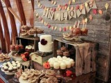 a rustic dessert table with lots of wooden stands and crates, a burlap bunting and a colorful leaf bunting and lots of tasty sweets
