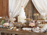 a rustic food display of a shabby chic table, vintage stands and cloches with sweets and some curtains behind the table
