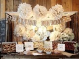 a vintage rustic dessert table with a burlap garland, white paper flowers, sweets in crates, baby’s breath in jars